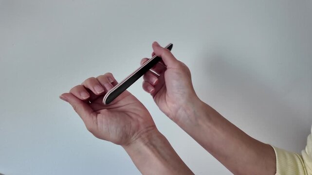 Woman doing manicure at home and filing her nails. Close-up of girl shaping fingernails with nail file during home beauty routine. Self-care, nail care