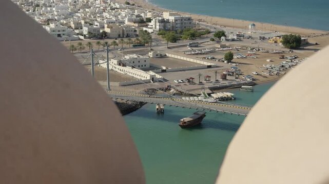 Slow Motion View of Sur Through Lookout Tower Buttresses, Cinematic Framed Panorama of Omani Coastal City