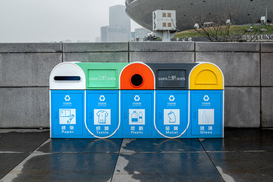 Modern recycling station in Shanghai, China featuring five color-coded compartments for Paper, Textile, Plastic, Metal, and Glass waste sorting, with Chinese and English bilingual labels, located in a