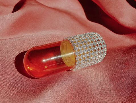 Glossy capsule with rhinestone shell on pink satin folds. Premium supplement concept with fashionable art direction.