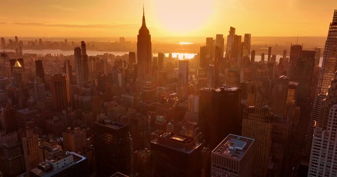 Golden hour in modern New York, USA. Orange light dazzles the dense urban panorama of Manhattan. Aerial view.