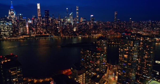 Approaching dark river waterscape flowing through New York, USA. Conic skyline of Manhattan at night from drone.