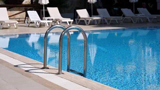 Modern swimming pool design with stainless steel ladder and non-slip drainage grate. Professional poolside construction, hotel infrastructure, safety standards and luxury outdoor lounge area, resort