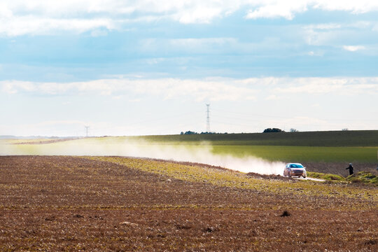 Coche de rally conduciendo r&aacute;pido por un camino de tierra creando una estela de polvo en el campo.