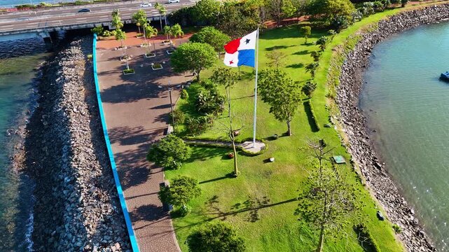 Descend over the shore with green park on and Panama flag on the pole. Historical center of Panama City, Republic of Panama, North America in the backdrop.