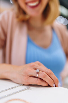 A smiling woman admires a luxury diamond engagement ring on her finger in a jewelry boutique showroom.