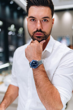 A stylish man in a white dress shirt poses with a luxury diver watch on his wrist while standing in a high-end jewelry store.
