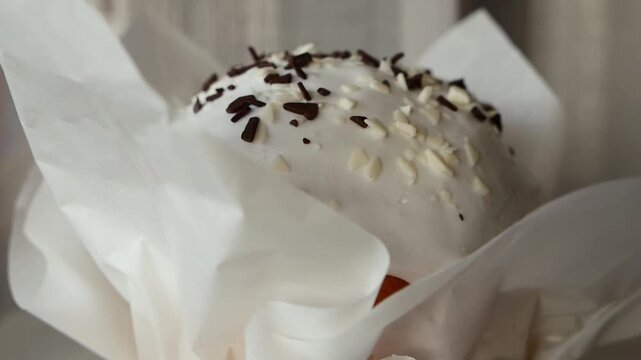 Traditional Easter kulich with white icing and chocolate sprinkles macro close up, festive homemade Easter bread cake in paper wrapper, sweet holiday pastry dessert.