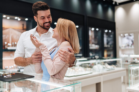 A smiling couple enjoys a romantic moment while looking at luxury rings and accessories in a modern jewelry store.