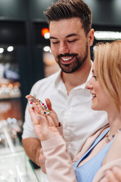A smiling young couple examines a colorful beaded bracelet together while shopping in a modern jewelry boutique.