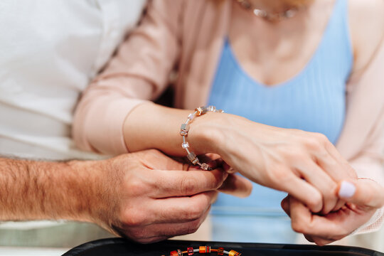 Close up of a man's hands fastening a stylish beaded bracelet on a woman's wrist during a special gift-giving moment.