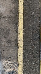 Fototapeta premium Close-up of asphalt pavement with a worn yellow road line, ideal for transportation themes, urban design, industrial backgrounds, and modern marketing visuals.