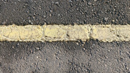 Fototapeta premium Close-up of asphalt pavement with a worn yellow road line, ideal for transportation themes, urban design, industrial backgrounds, and modern marketing visuals.