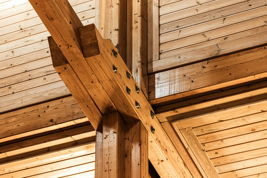 An exposed timber frame ceiling showcasing intersecting heavy wooden beams, visible metal bolts and tongue-and-groove planking, creating a warm, rustic architectural detail