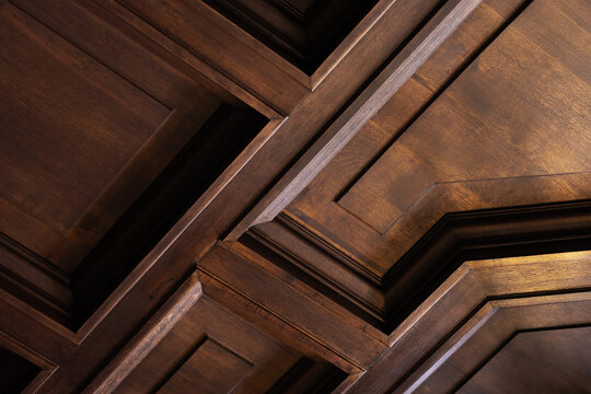 Close-up of a dark wood coffered ceiling showcasing geometric raised panels and rich brown stain. Classic interior architectural detail highlights texture, depth, craftsmanship and elegant atmosphere