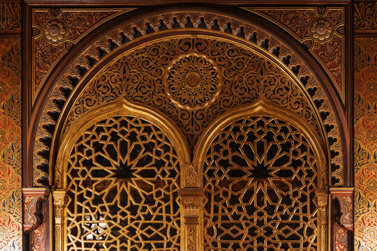 Ornate golden Moorish archway featuring intricate arabesque carvings, geometric lattice panels and detailed wood inlay that evoke historic Islamic architecture, skilled craftsmanship and decor