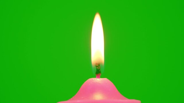Pink candle with a bright flickering flame stands against a vivid green background, creating a simple contrast scene with warm light, minimal composition, and clean studio style.
