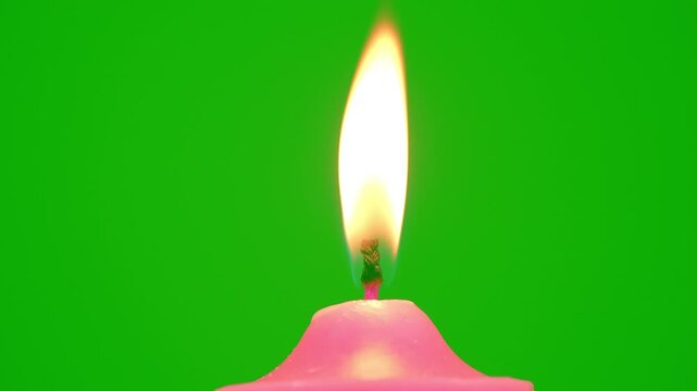 Pink candle with a bright flickering flame stands against a vivid green background, creating a simple contrast scene with warm light, minimal composition, and clean studio style.