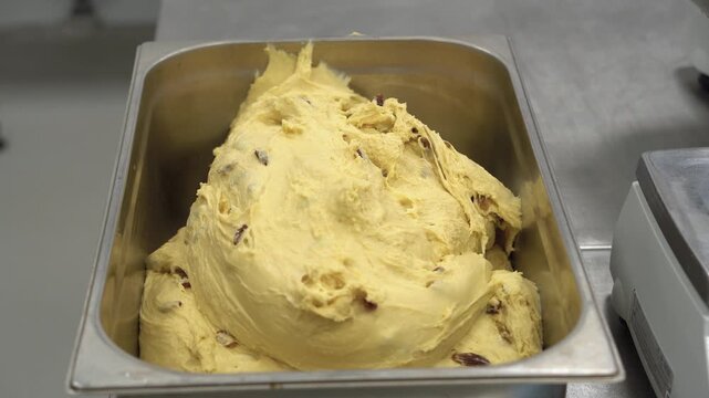 High-angle view of freshly prepared dough with plentiful raisins placed in a steel industrial tray. This footage captures the essential stage of the commercial baking process, highlighting ingredients
