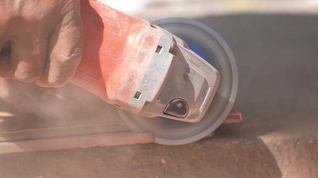 Close-up of a hand using an angle grinder to cut metal, sparks blurred in warm light, showing power tools, construction work, precision cutting, and industrial craftsmanship.