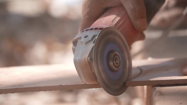 Close-up of a hand using an angle grinder to cut metal, sparks blurred in warm light, showing power tools, construction work, precision cutting, and industrial craftsmanship.