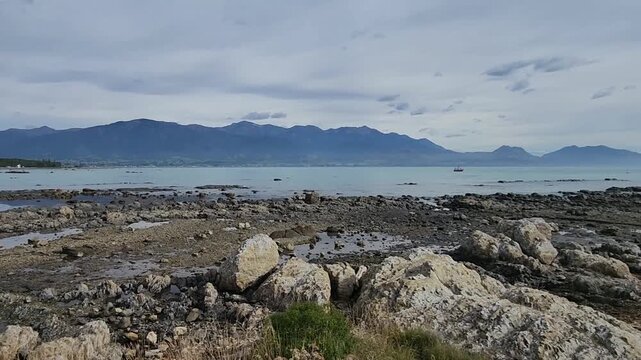 Kaikōura, New Zealand &mdash; Rocky Coastal Shoreline with Calm Blue Water, Low‑Tide Pools and Distant Mountain Range Under a Soft, Partly Cloudy Sky in a Peaceful Natural Landscape Setting 