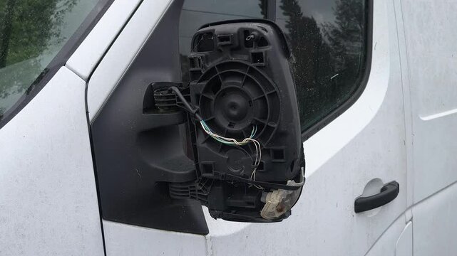 Broken car side mirror with exposed wires on white vehicle, close up damage detail, transportation accident concept, repair needed, safety risk, vandalism or collision aftermath.