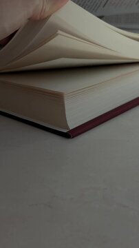 Slow motion tracking close up of hand flipping through pages of hardcover book on tabletop indoors with soft natural light
