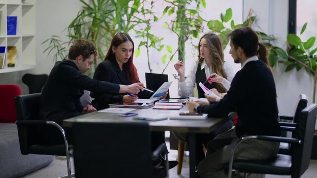 A group of business professionals holds a meeting, discussing important documents and strategies. The diverse team actively collaborates in a modern office environment.