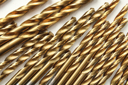 Collection of golden titanium coated metal drill bits of various sizes arranged diagonally, showcasing metallic texture and industrial pattern.