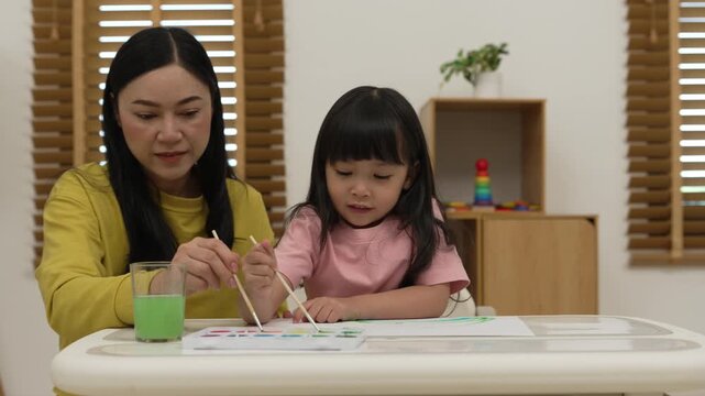happy mother and preschool child girl painting on paper with watercolor in pan at home