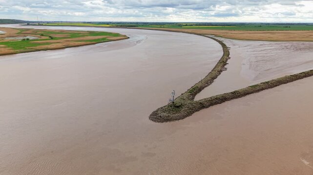 Aerial view of Trent Falls confluence with a stone breakwater and navigation beacon under a cloudy sky in Goole, United Kingdom.