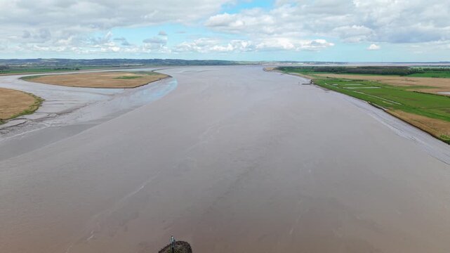 Aerial view of Trent Falls where the River Ouse and River Trent meet, featuring muddy waters and lush green riverbanks under a cloudy sky in Goole, United Kingdom.
