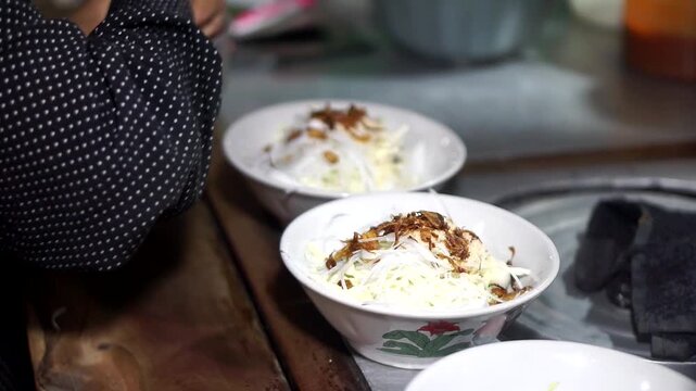 The hands of street vendors selling Indonesian specialties prepare soto lontong in bowls using simple and quick techniques.