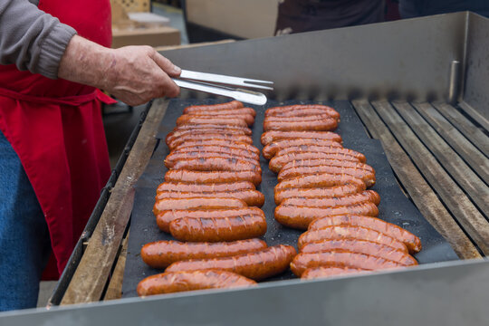 Close up of bartender using tongs to flip sizzling sausages on a flat grill