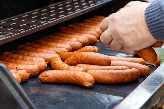 Close up of bartender using tongs to flip sizzling sausages on a flat grill