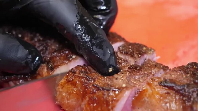 A detailed, macro shot of a professional chef wearing black nitrile gloves using a sharp stainless steel knife to slice through a perfectly seared, juicy grilled steak. The meat shows a rich carameliz