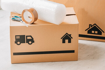 Stack of cardboard moving boxes with truck and house icons, bubble wrap, and packing tape on top,...