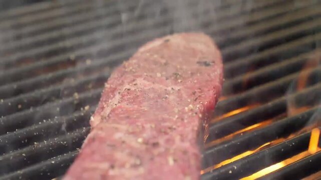 Close-up cinematic shot of a premium, highly-marbled slice of raw A5 Japanese Wagyu beef sizzling on a hot grill. The footage highlights the intense white fat marbling (shimofuri) and the red meat as 
