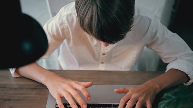 High angle top view of young male student working on laptop, typing on keyboard, online studying, freelance work, remote job, productivity and digital lifestyle concept.