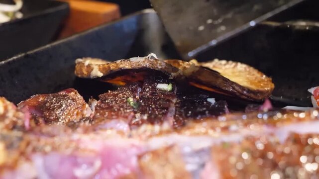 A close-up, high-definition video of a thick-cut, premium T-bone or ribeye steak being seasoned and grilled on a hot barbecue. The meat is juicy and perfectly cooked with a pink center, capturing the 