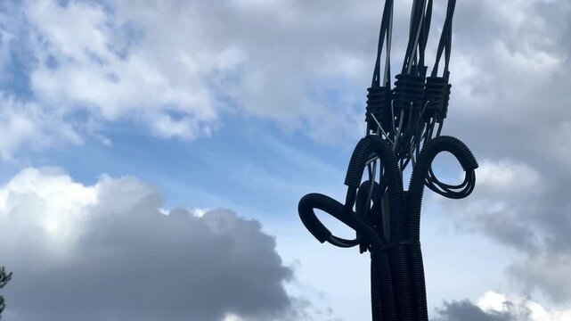 Wires and pipes connect in the sky above a cloudy landscape during the afternoon