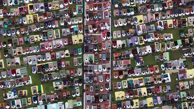 Aerial view of a large crowd of people praying on colorful mats laid out on a green field during a communal gathering in Klaten, Jawa Tengah, Indonesia.