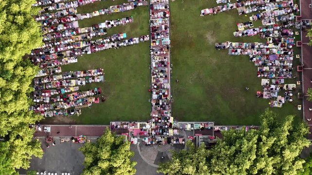 Aerial view of people gathered on a green lawn with mats and stalls surrounded by lush trees in Klaten, Jawa Tengah, Indonesia.
