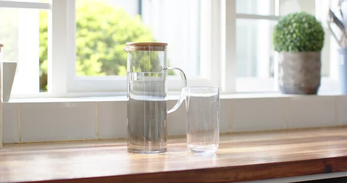 Glass pitcher and glass staying centered on wood worktop while breeze moving leaves light shifting