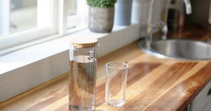 Carafe and glass are remaining on countertop as camera is refocusing and water is rippling