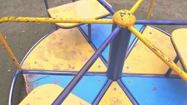 A spinning yellow and blue playground carousel in a public park. Nostalgic childhood, outdoor play, park leisure.