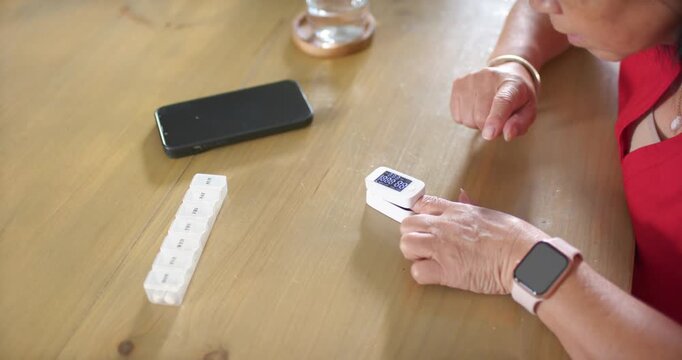 Senior Asian woman in red top after cell alert tapping white device, checking pillbox, copy space