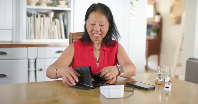 Senior Chinese woman finishing blood pressure check at home, removing cuff and arranging monitor