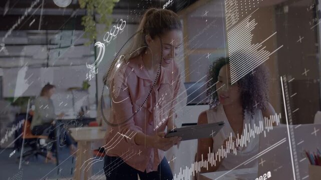 Standing woman showing tablet in office, HUD charts appearing over laptop while peer reviewing data